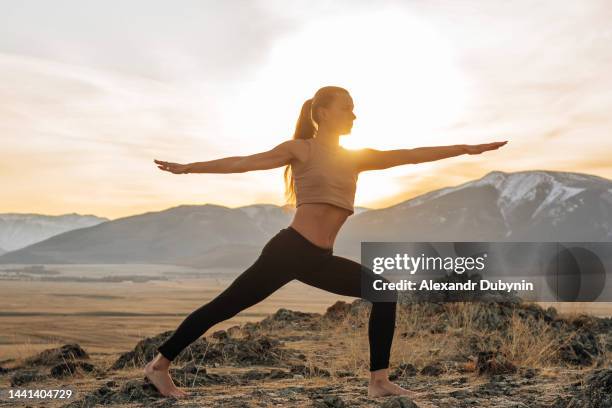 beautiful young woman doing yoga in the mountains in the rays of the setting sun - woman stretching sunset stock-fotos und bilder