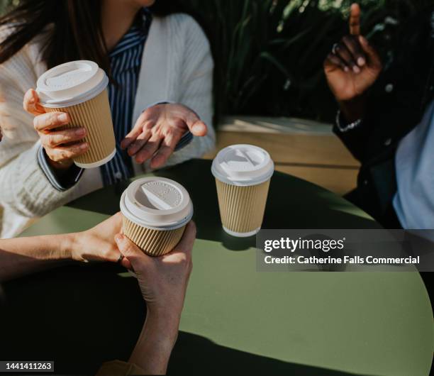 a group of colleagues sit at a table outdoors and enjoy some takeaway coffees - takeaway coffee cup stock-fotos und bilder