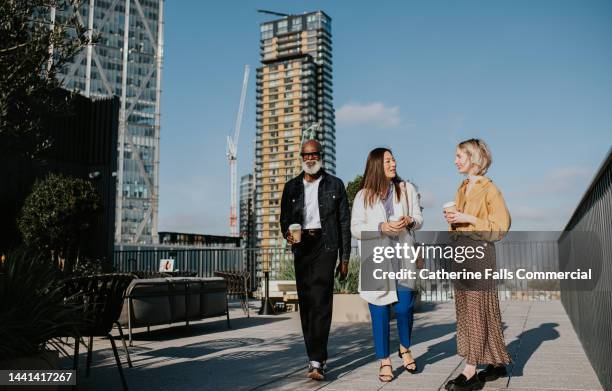 three people in smart-casual business attire walk together on a roof top, surrounded by high rise buildings - apartment tour stock pictures, royalty-free photos & images