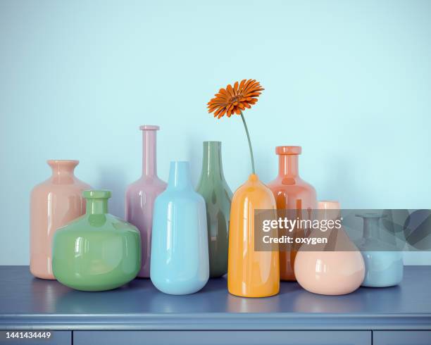 multicolored bottles vases from glass with one daisy flower on blue dresser and blue wall abstract background. 3d rendering. vintage retro colored - bureau vintage stock-fotos und bilder