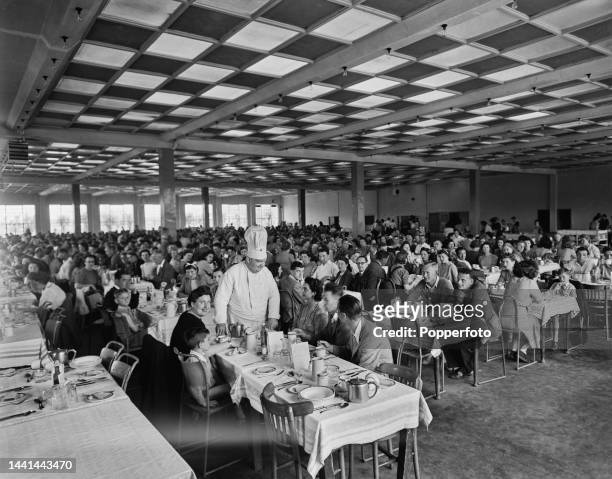 Holidaymakers, guests and diners are greeted by a chef as they enjoy a meal in the large dining room canteen at Butlin's Filey holiday camp near the...