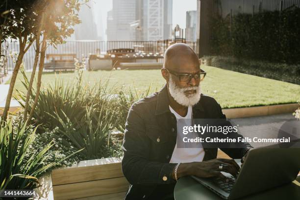 a man sits outside on a rooftop terrace and uses a laptop - dachterasse stock-fotos und bilder