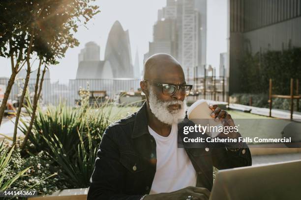 a man sits outside on a rooftop terrace and uses a laptop - al fresco dining stock pictures, royalty-free photos & images