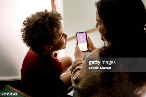 son looking at mother holding smart phone with home automation app - copilot ストックフォトと画像