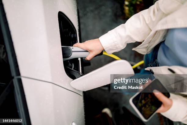 directly above shot of woman charging electric car - vehículo híbrido fotografías e imágenes de stock