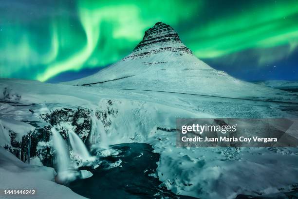 northern lights (aurora borealis) dancing over the frozen waterfall of kirkjufellfoss in winter covered in ice and snow (snowcapped mountain) with kirkjufell mountain in the background, snaefellsnes, iceland - volcanic terrain stock pictures, royalty-free photos & images