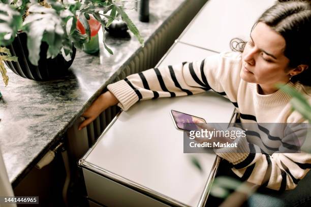 high angle view of woman checking temperature of radiator through smart phone application at home - radiator stock pictures, royalty-free photos & images