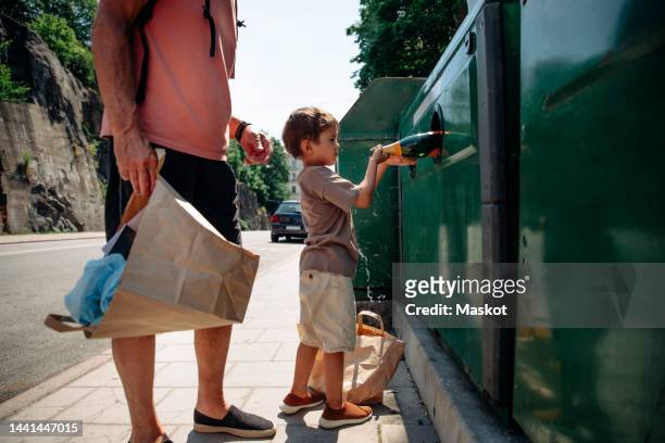 side view of boy trashing bottle in garbage bin while standing with grandfather - bottle bank stock pictures, royalty-free photos & images