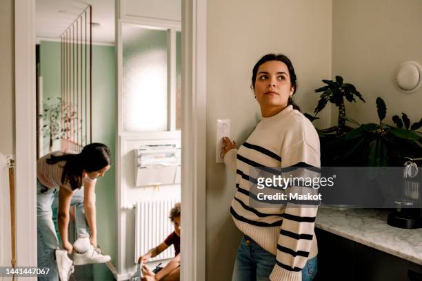 woman turning off light switch while standing near doorway at home - turn off light stock pictures, royalty-free photos & images