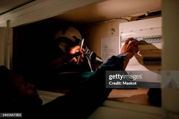 man turning on switch from fuse box using smart phone torch during blackout - fuse box stockfoto's en -beelden