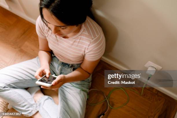 high angle view of girl using smart phone while sitting by wall at home - social media addiction stock pictures, royalty-free photos & images