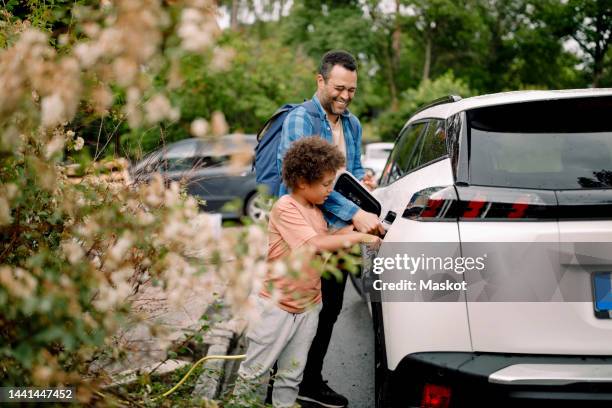 smiling man with son charging electric car - vehículo híbrido fotografías e imágenes de stock