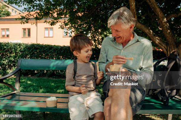 happy grandfather and grandson enjoying ice cream while sitting on bench - grandfather and grandson stock pictures, royalty-free photos & images