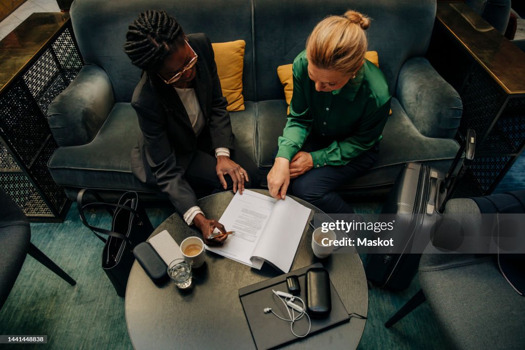 Businesswomen discussing over contract while sitting in hotel lounge