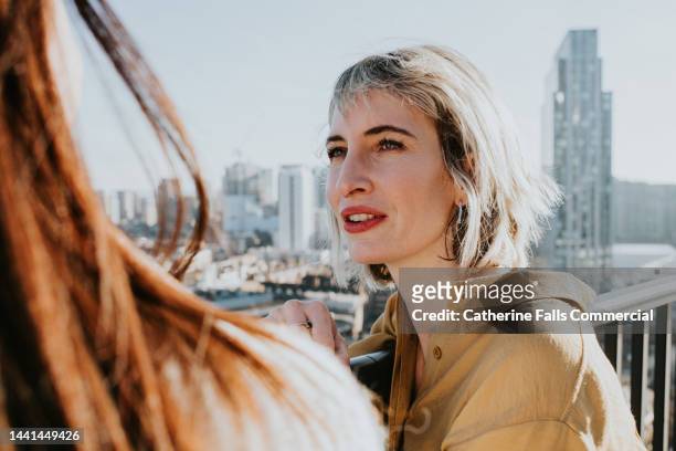 a woman leans up against a balcony and chats to another woman - enterprise stock pictures, royalty-free photos & images