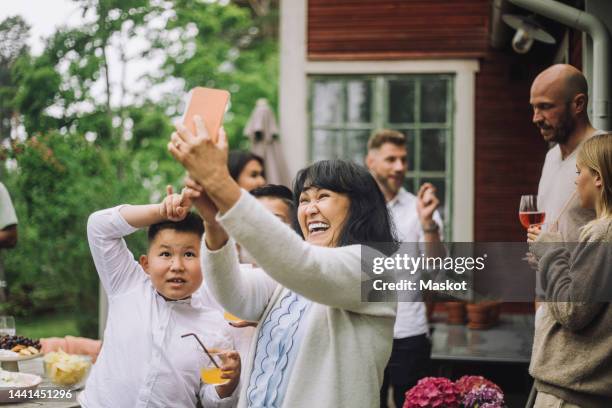 happy grandmother taking selfie through smart phone with grandchildren at party - europe de l'ouest photos et images de collection