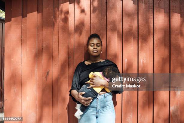 woman with eyes closed breastfeeding toddler daughter in front of wall on sunny day - 2 5 mois photos et images de collection