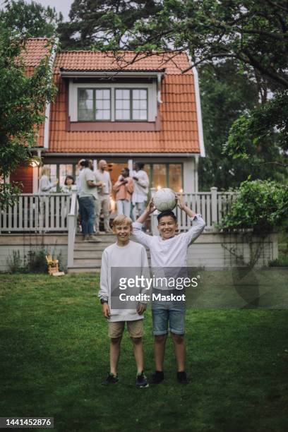 playful boys with soccer ball standing in back yard with family on porch in background - before the party stock pictures, royalty-free photos & images