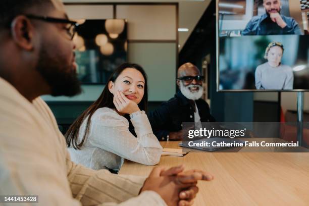 an in-person meeting between colleagues with others dialling in remotely - conference room screens stock pictures, royalty-free photos & images