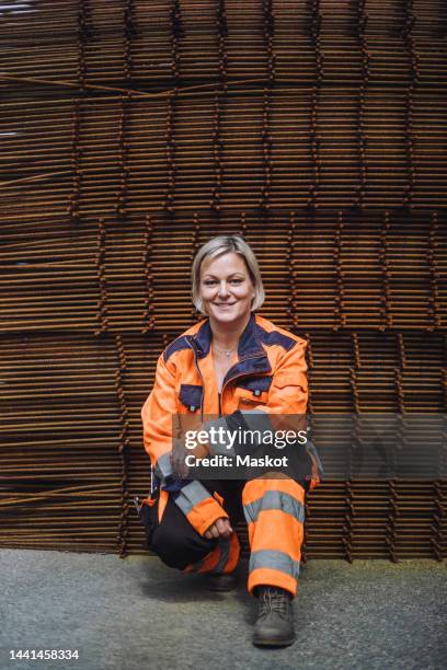 full length portrait of smiling female construction worker crouching at site - laborer stock-fotos und bilder