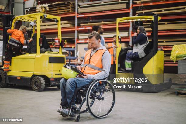 full length of male carpenter with disability using digital tablet sitting on wheelchair in warehouse - schreiner tablet stock-fotos und bilder