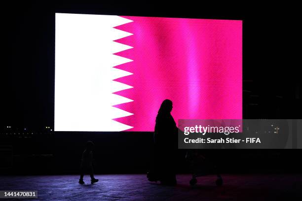 Woman and child walk past a digital screen showing the flag of Qatar ahead of the FIFA World Cup Qatar 2022 at Katara Village on November 14, 2022 in...