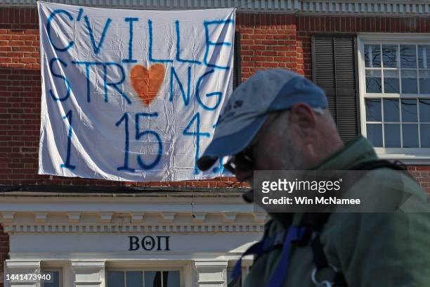 Pedestrian stands in front of a fraternity house with a banner memorializing three University of Virginia football players killed during an overnight...