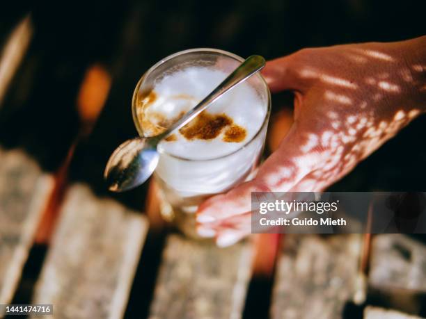 hand and hot latte macchiato coffee in a glass on a table. - milchschaum stock-fotos und bilder