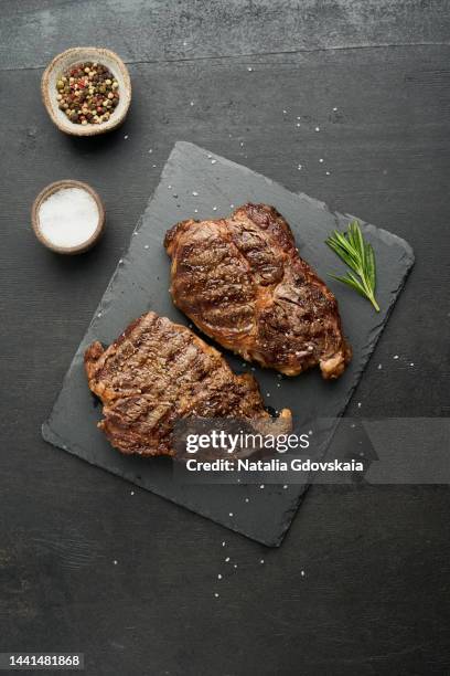 ribeye, rib eye steak. keto ketogenic diet, beef meat, grilled fried striploin on cutting board on dark brown table. paleo food recipe. tender top blade beefsteaks with rosemary - steak stock-fotos und bilder