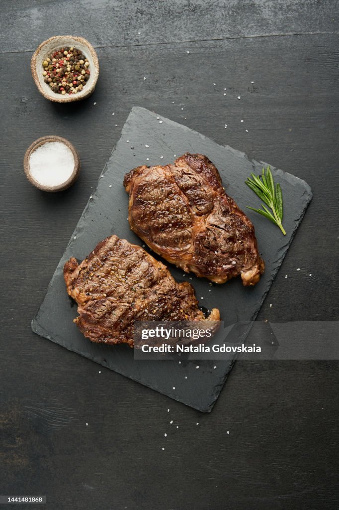 Ribeye, rib eye steak. Keto ketogenic diet, beef meat, grilled fried striploin on cutting board on dark brown table. Paleo food recipe. Tender top blade beefsteaks with rosemary