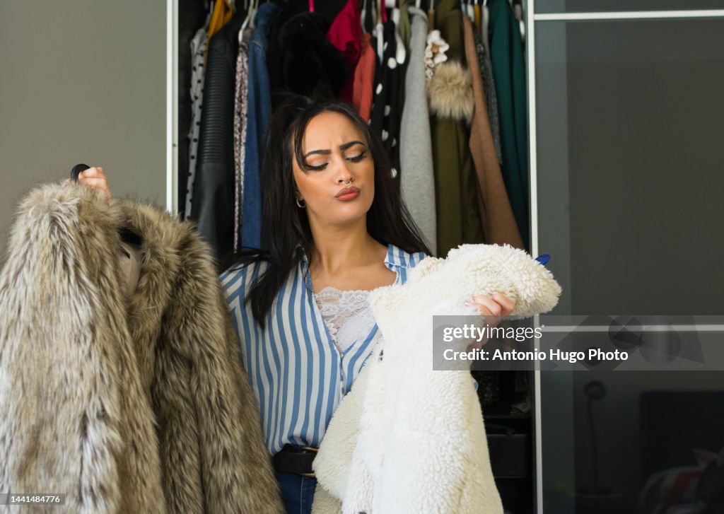 Young brunette woman with make-up looking at the clothes in her wardrobe and deciding which clothes to wear. Women's fashion concept.