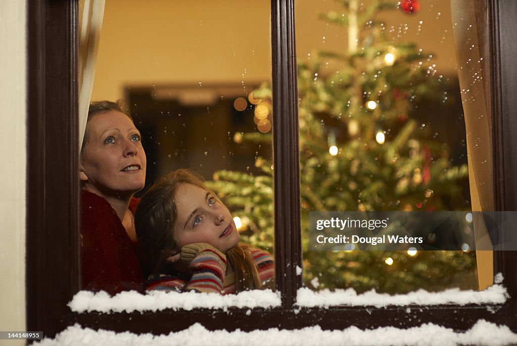 Girl and mother gazing out of window at christmas.