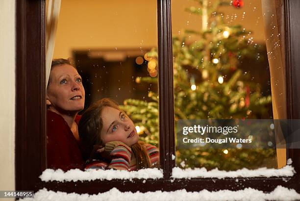 girl and mother gazing out of window at christmas. - snow window stock pictures, royalty-free photos & images