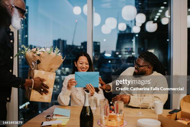 office workers lavish attention and praise on a colleague, presenting a card and flowers to her as she smiles - draft after party stock-fotos und bilder