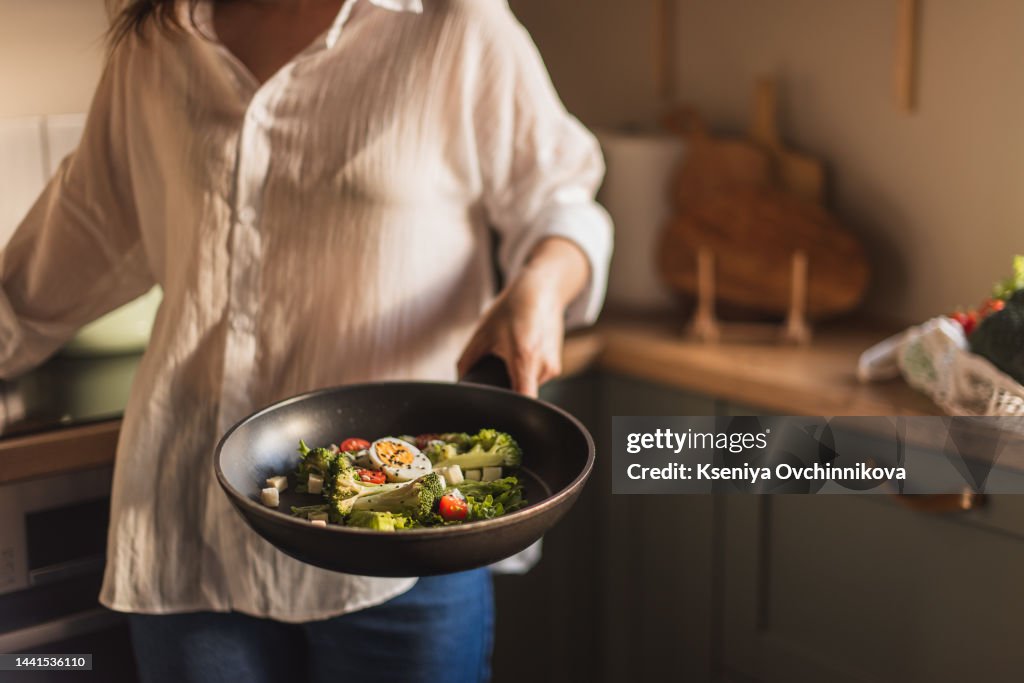 Caucasian senior woman hand with fork stirring frying vegetables in frying pan, close-up