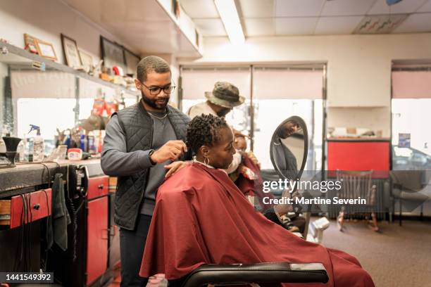 black customers receive a haircut from barbers at a black owned barbershop - african american hair salon stock pictures, royalty-free photos & images
