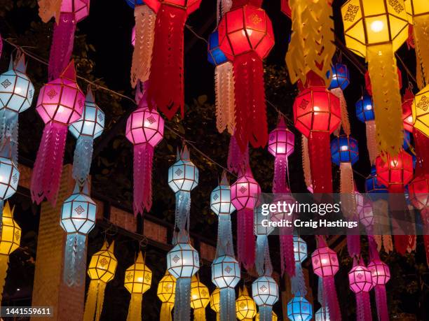 bangkok loi krathong thai chinese style lanterns of many colours on display in temple. colourful illuminations for ancient style lamps shine across the street. establishing shot of south east asia celebrations and festivals - buddha's birthday stock-fotos und bilder