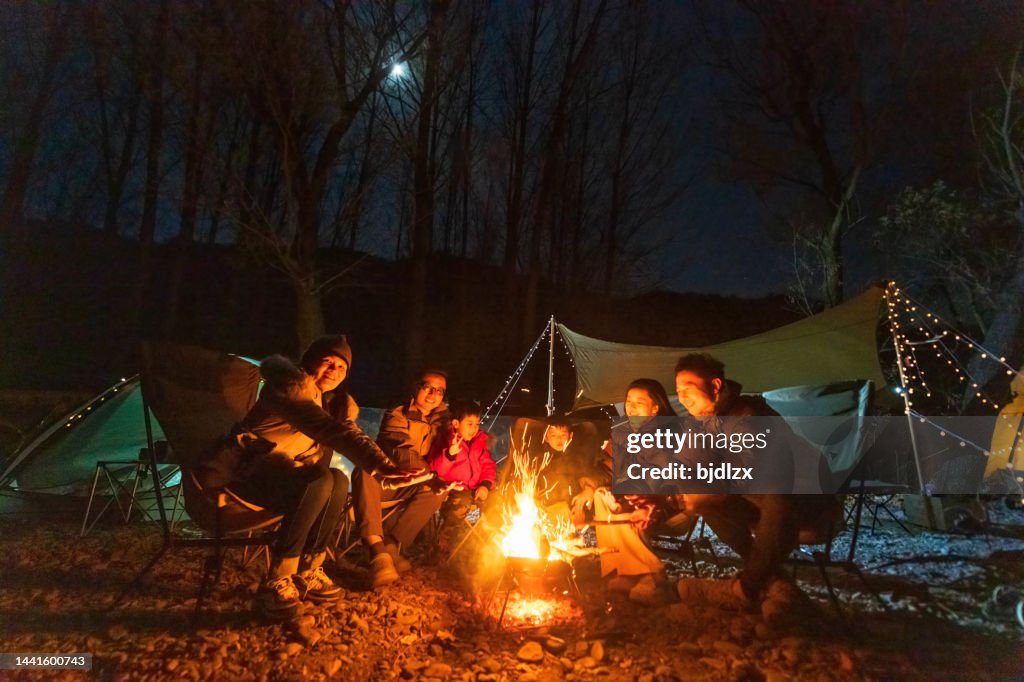 A group of campers celebrate around the campfire in late autumn night