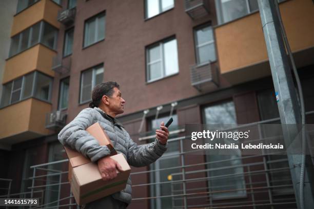 delivery of goods. elderly male courier with parcel boxes and smartphone. tradesman finding customer phone number. - tradesman real people man stock pictures, royalty-free photos & images