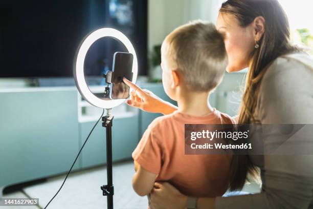 mother live streaming with son on smart phone with ring light at home - influencer mom stock pictures, royalty-free photos & images