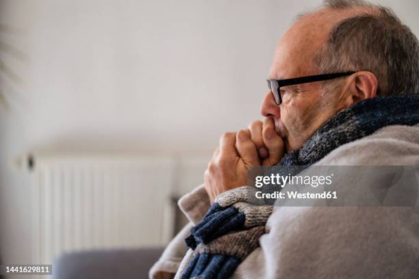 senior man wrapped in blanket feeling cold at home - wrapped in a blanket stock pictures, royalty-free photos & images