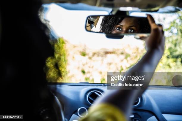 selective focus shot of young woman adjusting a rear view mirror in her new car - black mirror imagens e fotografias de stock