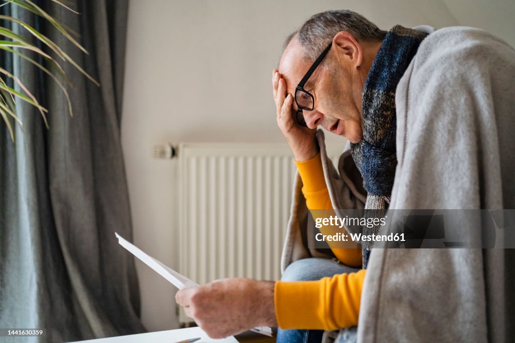 Worried man with head in hand looking at heating bill in home
