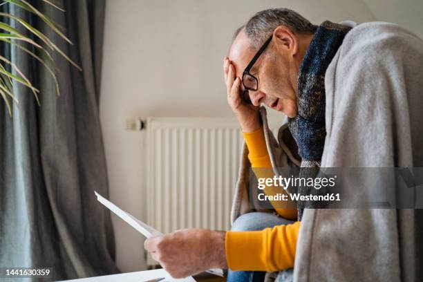 worried man with head in hand looking at heating bill in home - energy bill stock pictures, royalty-free photos & images