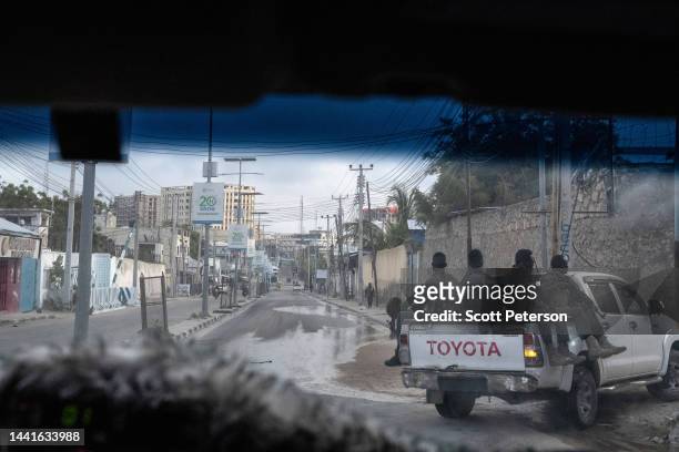 Armed Somali security guards escort an armored vehicle through the city, in dawn light photographed through a window, on streets that are threatened...