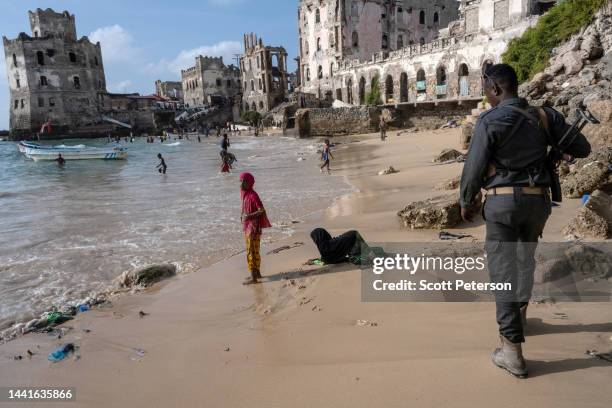 An armed Somali guard walks amid beach where children swim and play at the old port and traditional lighthouse, as famine looms over Somalia with an...