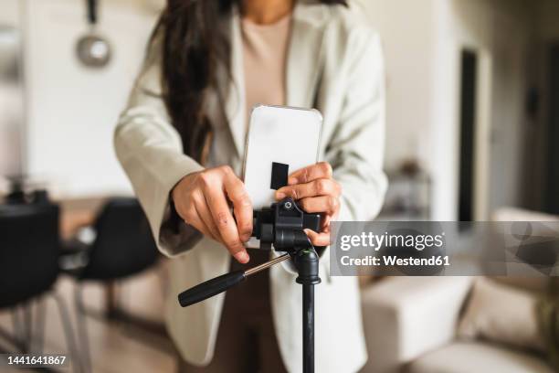 woman adjusting smart phone on tripod at home - stativ stock-fotos und bilder