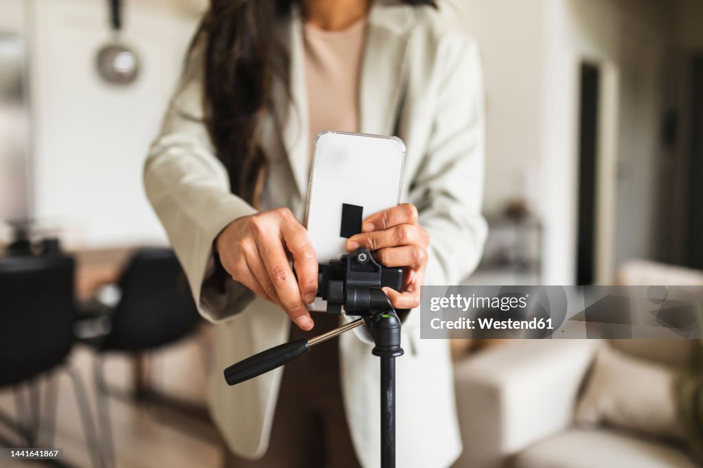 Woman adjusting smart phone on tripod at home