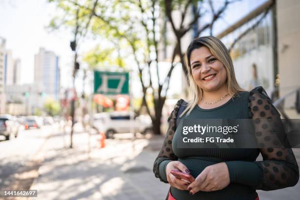 portrait of a paraguayan mid adult woman smiling in the city while using mobile phone - paraguayan people stock pictures, royalty-free photos & images