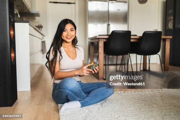 happy woman with puzzle cube sitting on carpet at home - rubics cube stock pictures, royalty-free photos & images